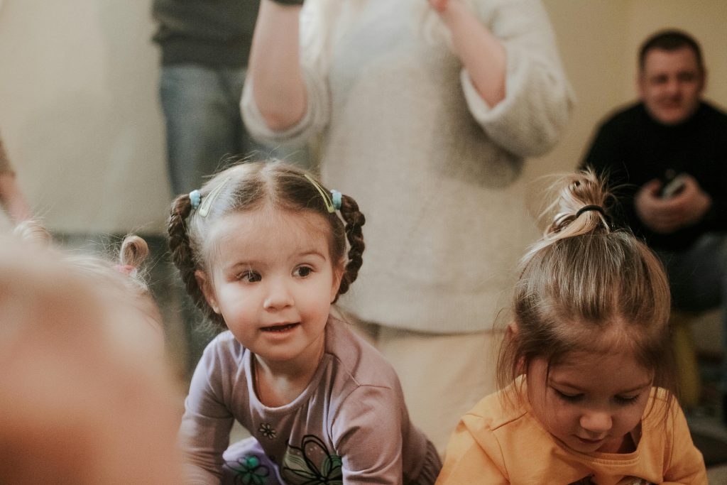 Two young girls enjoy a playful moment inside, captured in warm, cozy tones.